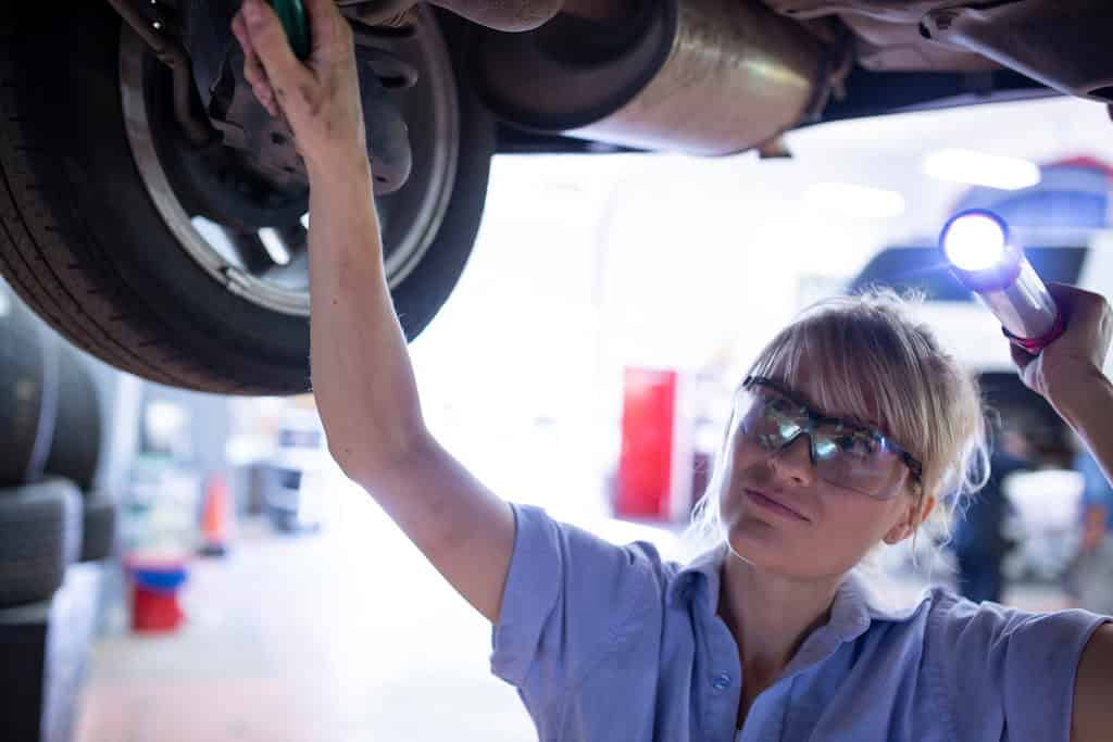 Female mechanic attends to a car that has been lifted by a mobile bench