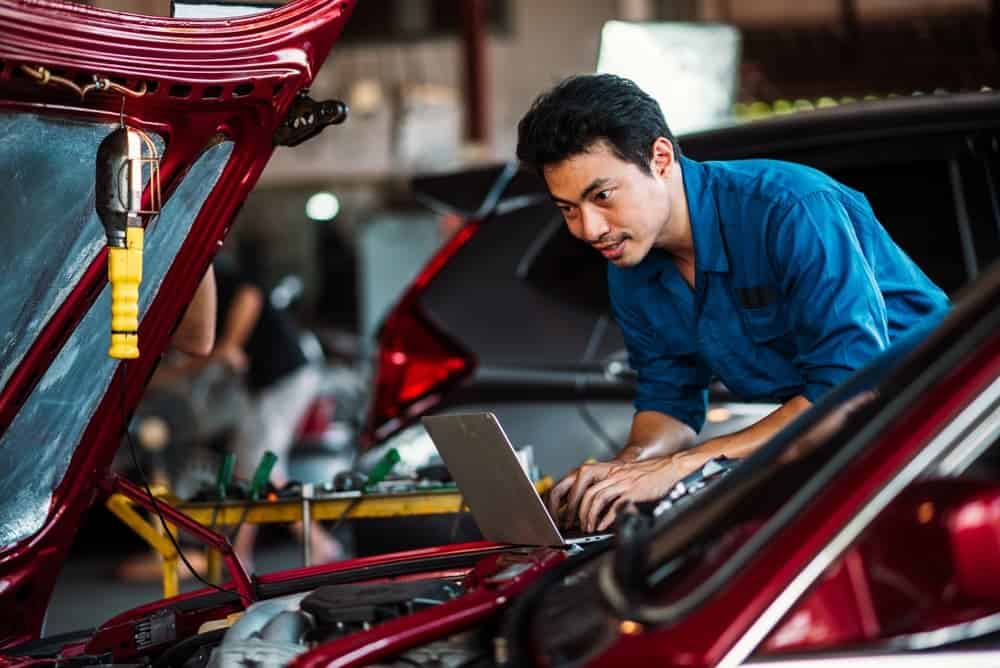 Un hombre usando software de IA para reparación de colisiones mostrando datos 3D de estructuras de vehículos con IA en su portátil.