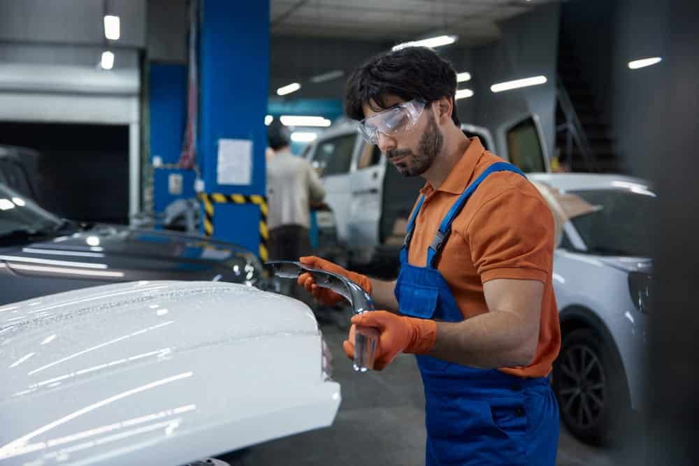 Técnico de carrocería automotriz reparando el capó de un automóvil siguiendo técnicas profesionales de reparación de carrocería