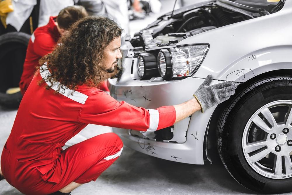A collision repair technician working on a vehicle secured by frame-pulling clamps