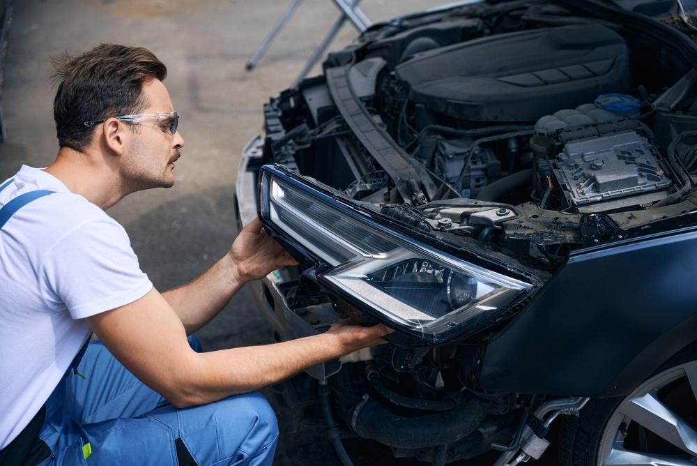 자동차 구조적 손상 수리 중 헤드라이트를 탈거하는 기술자
