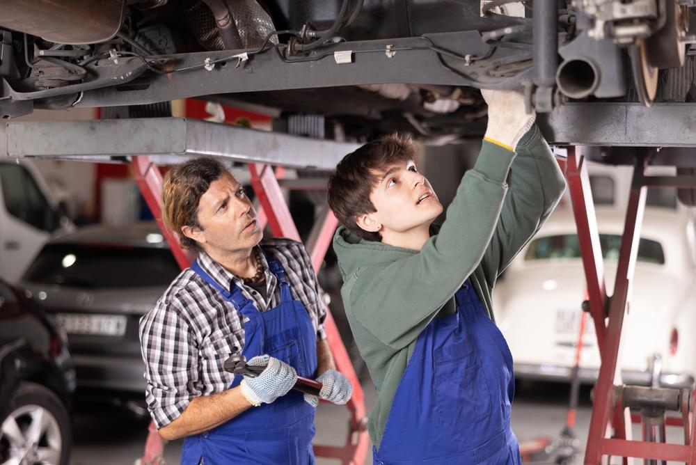Two technicians working with a drive-on bench with dual lifting systems in a professional collision repair body shop.